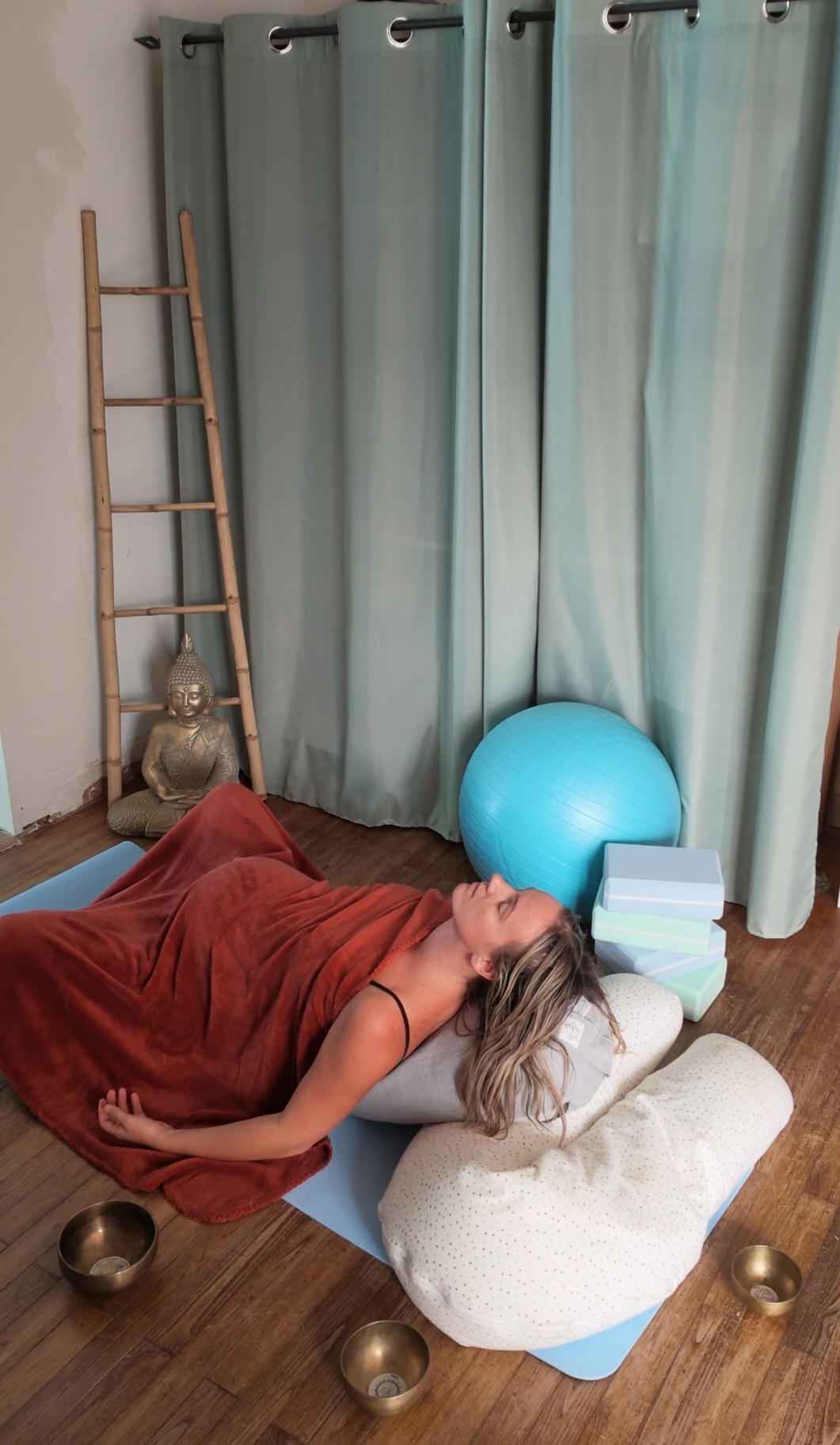 Posture de yin yoga allongée sur un bolster, entourée de bols tibétains, pour une séance de yoga femme enceinte à Rezé.